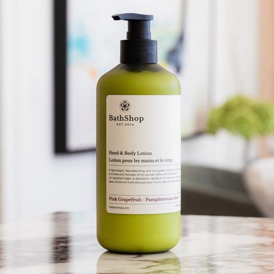 Green bottle of The Bath Shop hand and body lotion on a marble surface with a blurred background